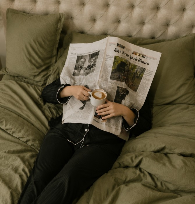 Hóspede a ler o jornal e a tomar café numa cama OMID Hotels